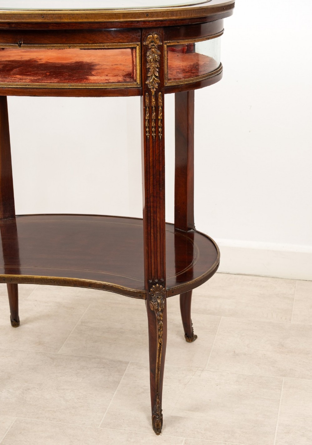 An antique oval mahogany bijouterie table featuring curved glass sides, an undertier shelf, and ornate gilt-bronze mounts. View V