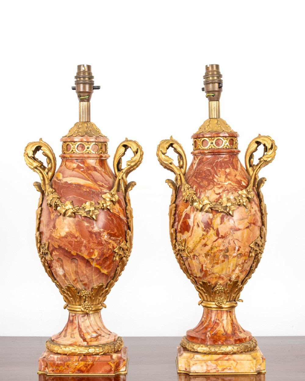 A pair of late nineteenth-century French urn-form table lamps crafted from veined red marble with gilt bronze scroll handles and floral garlands.