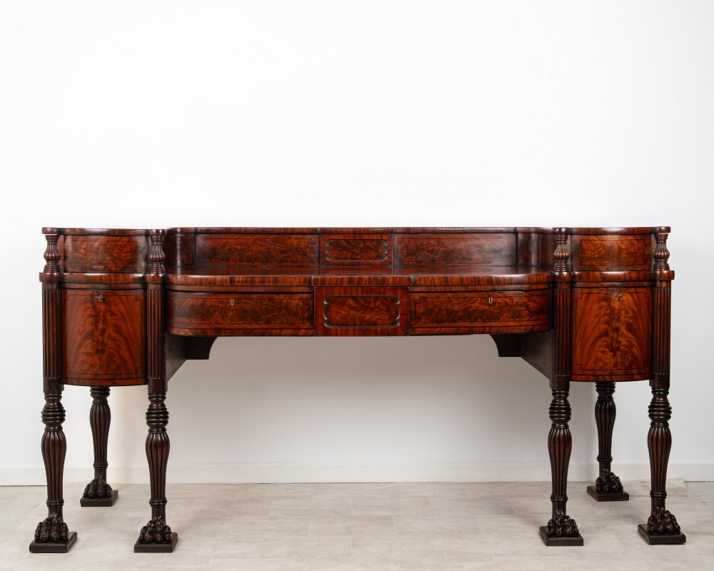 A Regency flame mahogany sideboard featuring reeded turned legs, carved paw feet, multiple storage drawers, and a raised back gallery rail.