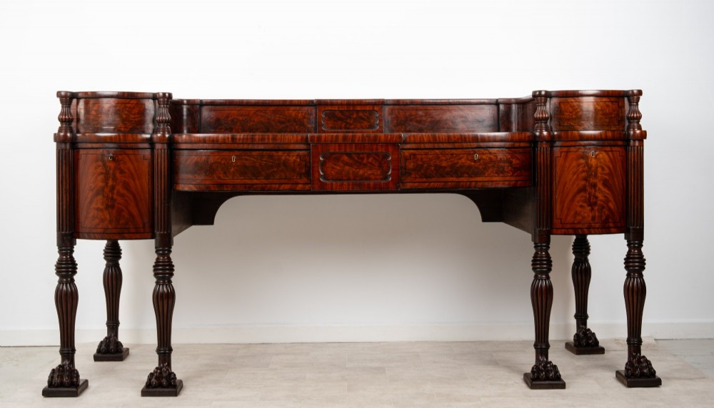 A Regency flame mahogany sideboard featuring reeded turned legs, carved paw feet, multiple storage drawers, and a raised back gallery rail. View II