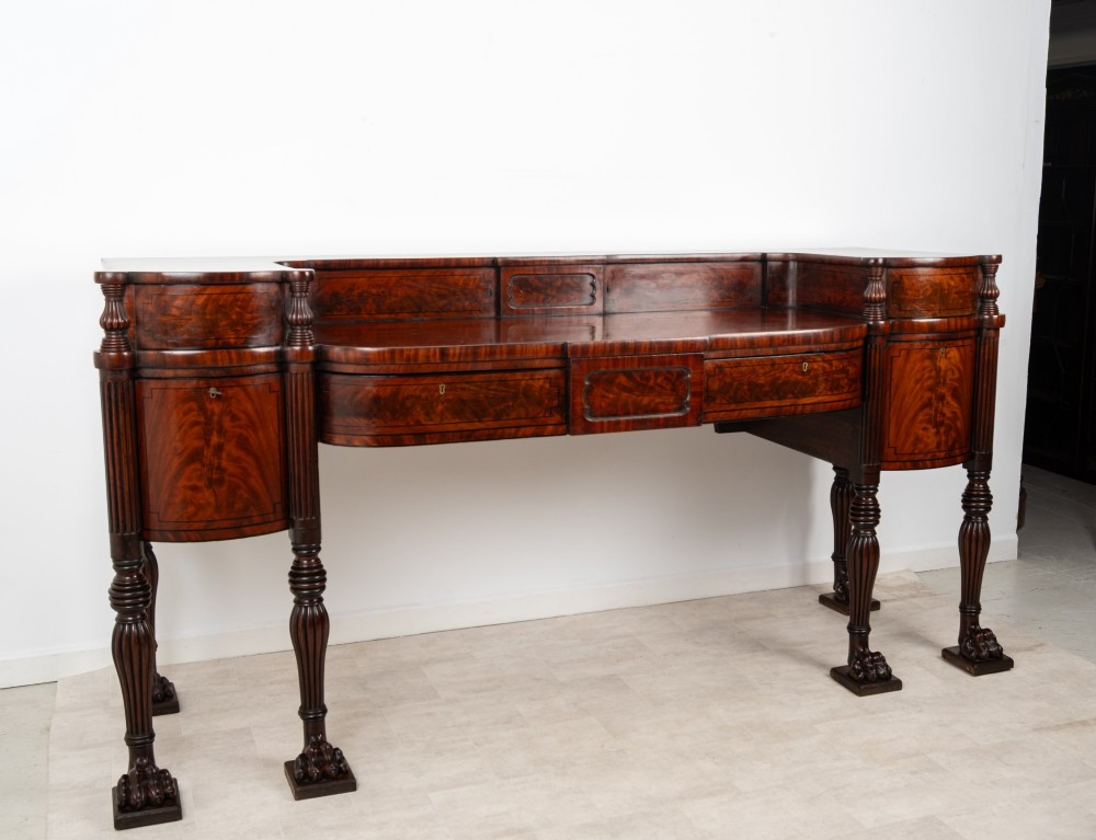 A Regency flame mahogany sideboard featuring reeded turned legs, carved paw feet, multiple storage drawers, and a raised back gallery rail. View IV