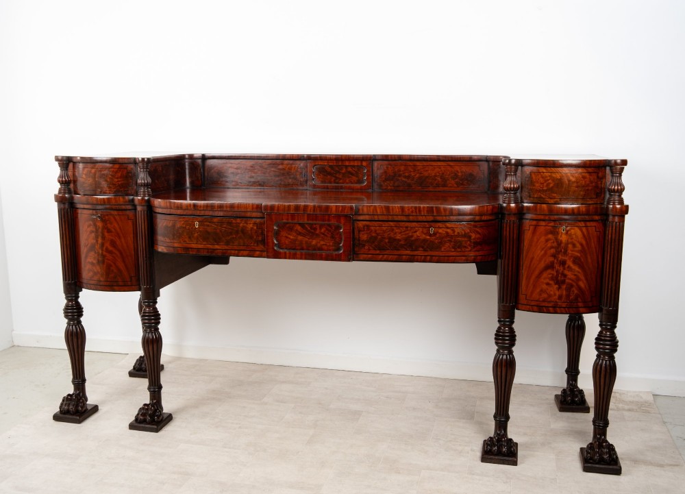 A Regency flame mahogany sideboard featuring reeded turned legs, carved paw feet, multiple storage drawers, and a raised back gallery rail. View V