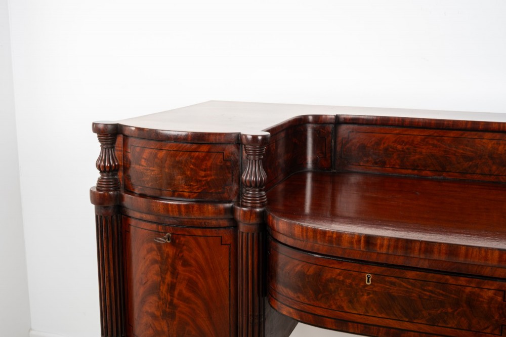 A Regency flame mahogany sideboard featuring reeded turned legs, carved paw feet, multiple storage drawers, and a raised back gallery rail. View VI