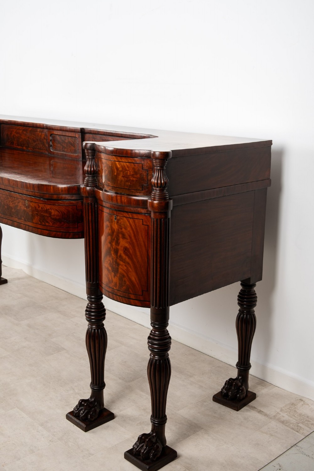 A Regency flame mahogany sideboard featuring reeded turned legs, carved paw feet, multiple storage drawers, and a raised back gallery rail. View XI