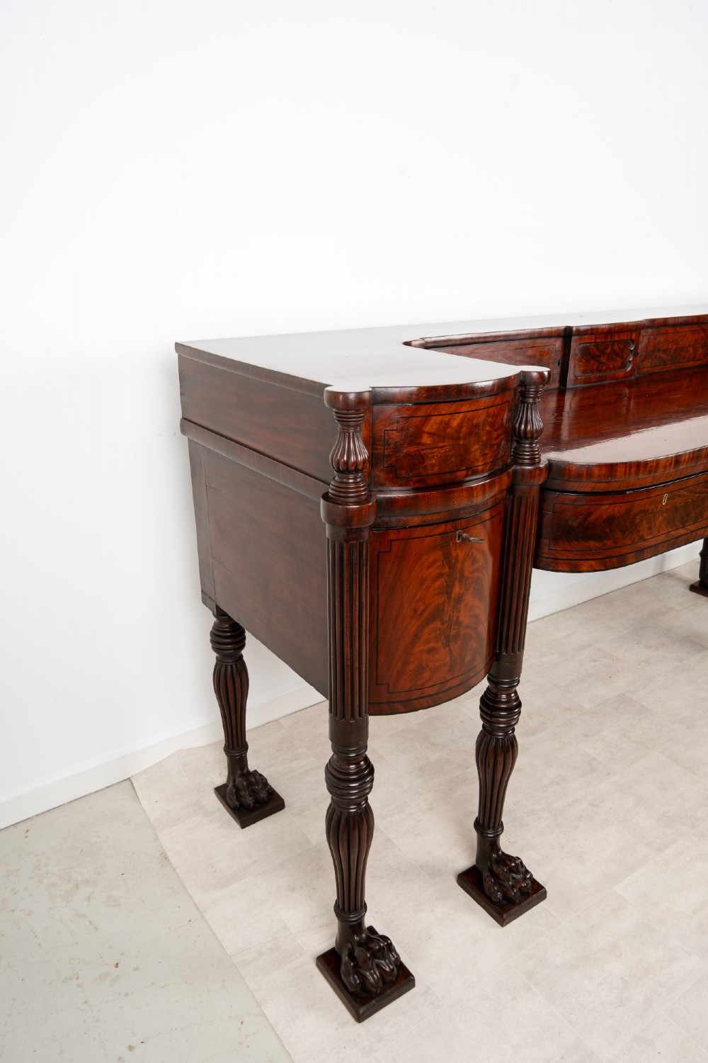 A Regency flame mahogany sideboard featuring reeded turned legs, carved paw feet, multiple storage drawers, and a raised back gallery rail. View XII