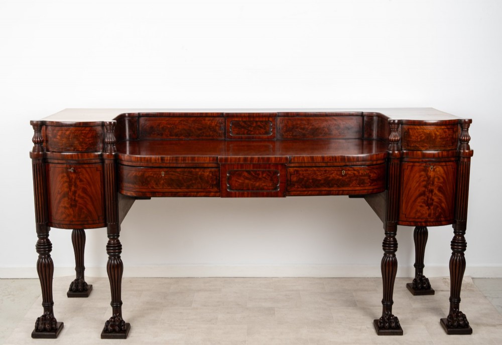 A Regency flame mahogany sideboard featuring reeded turned legs, carved paw feet, multiple storage drawers, and a raised back gallery rail. View XIV