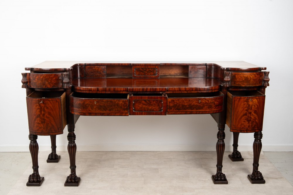 A Regency flame mahogany sideboard featuring reeded turned legs, carved paw feet, multiple storage drawers, and a raised back gallery rail. View XV