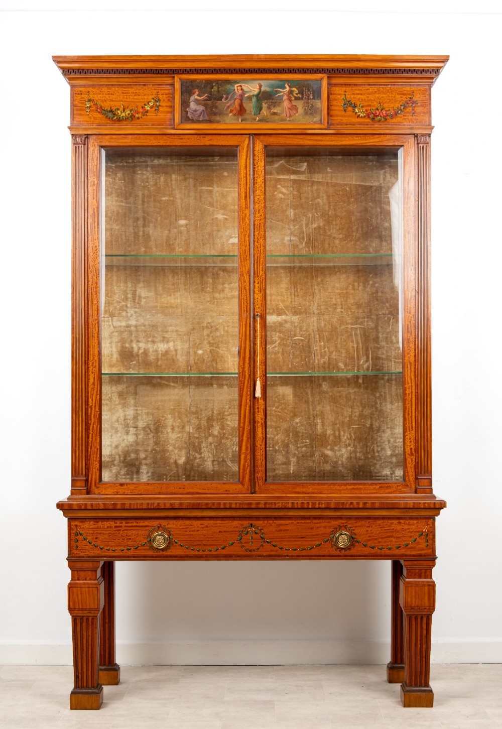 An Edwardian satinwood display cabinet on stand featuring glazed double doors, hand-painted floral garlands, and a central classical figural panel.