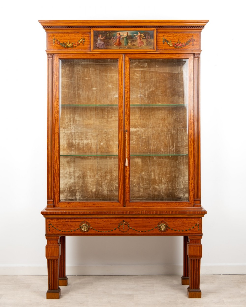 An Edwardian satinwood display cabinet on stand featuring glazed double doors, hand-painted floral garlands, and a central classical figural panel. View II