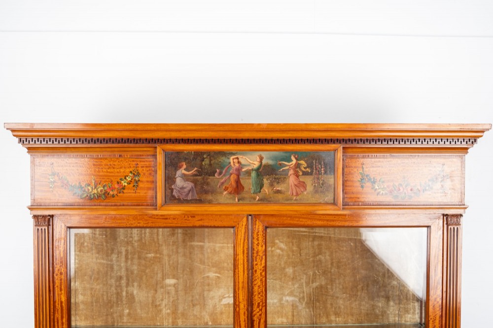 An Edwardian satinwood display cabinet on stand featuring glazed double doors, hand-painted floral garlands, and a central classical figural panel. View IV