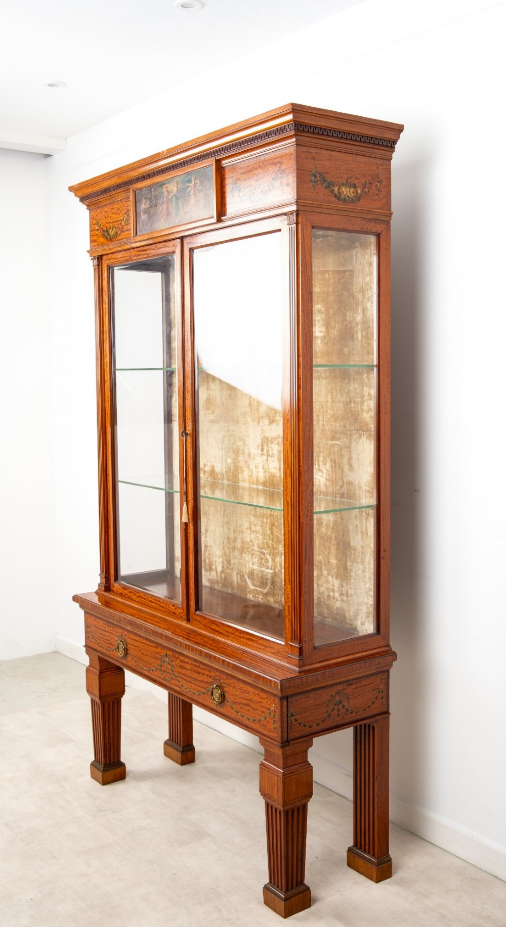 An Edwardian satinwood display cabinet on stand featuring glazed double doors, hand-painted floral garlands, and a central classical figural panel. View VI
