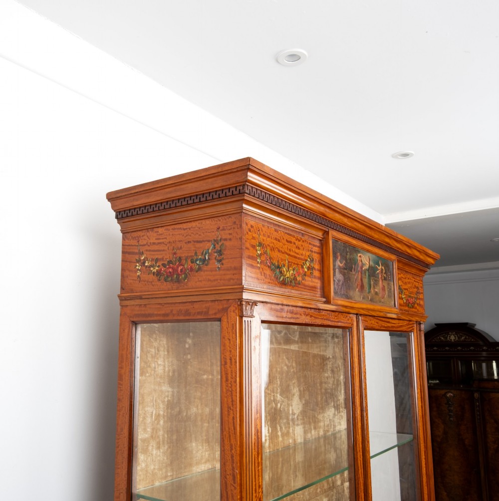 An Edwardian satinwood display cabinet on stand featuring glazed double doors, hand-painted floral garlands, and a central classical figural panel. View VIII