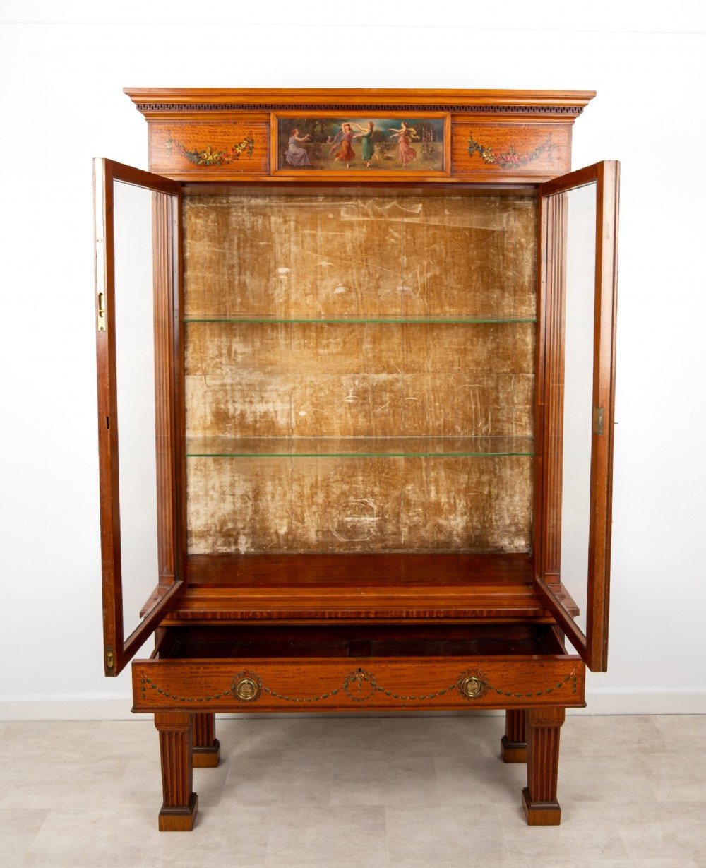 An Edwardian satinwood display cabinet on stand featuring glazed double doors, hand-painted floral garlands, and a central classical figural panel. View IX