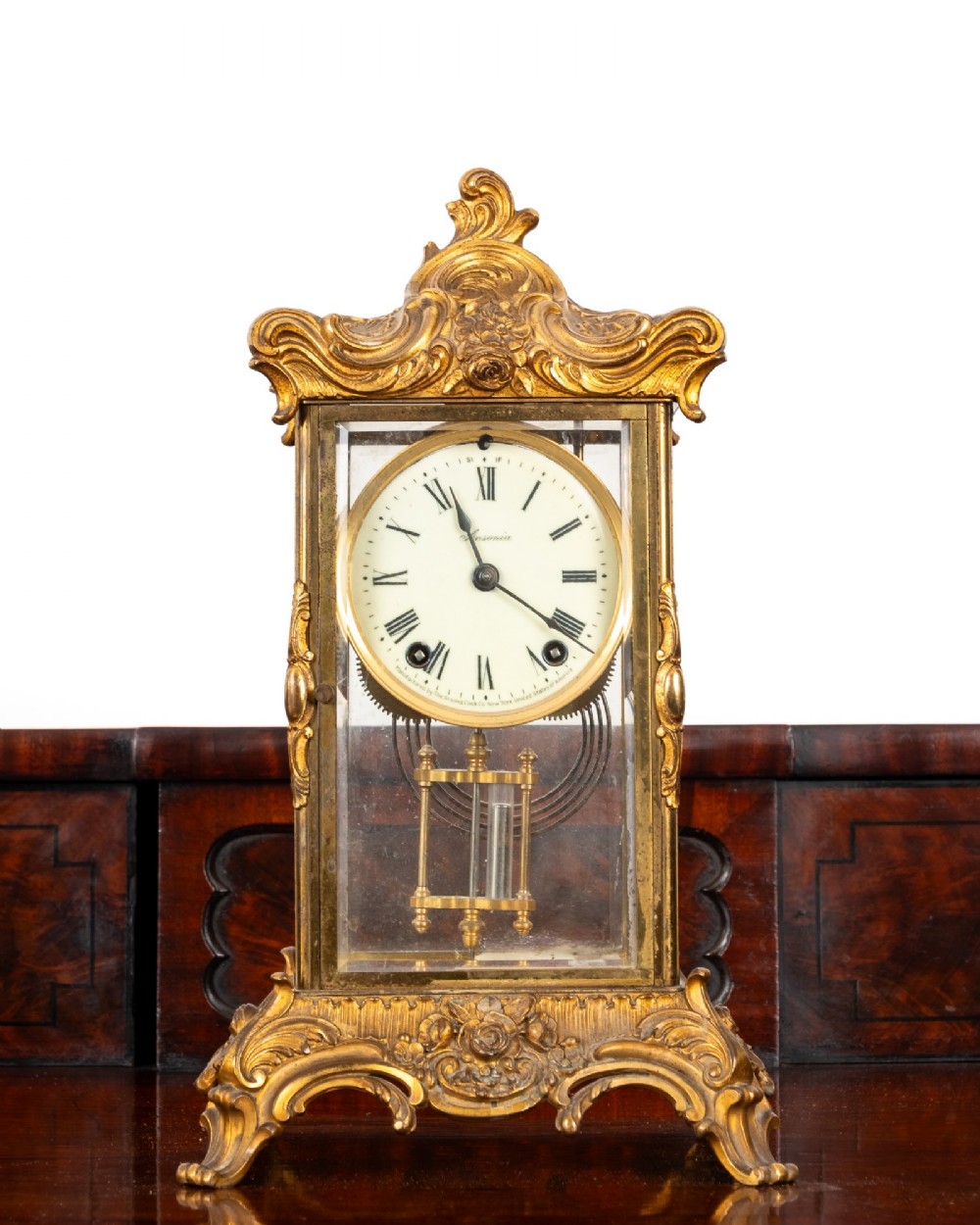 A late 19th-century Rococo Revival gilt bronze crystal regulator mantel clock featuring four bevelled glass panels, ornate scrollwork casting, an enamel dial with Roman numerals, and a visible mercury-style pendulum. View II