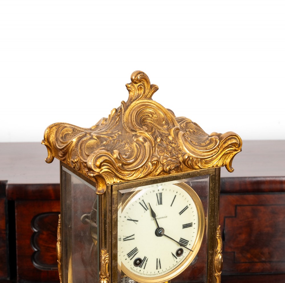 A late 19th-century Rococo Revival gilt bronze crystal regulator mantel clock featuring four bevelled glass panels, ornate scrollwork casting, an enamel dial with Roman numerals, and a visible mercury-style pendulum. View IV