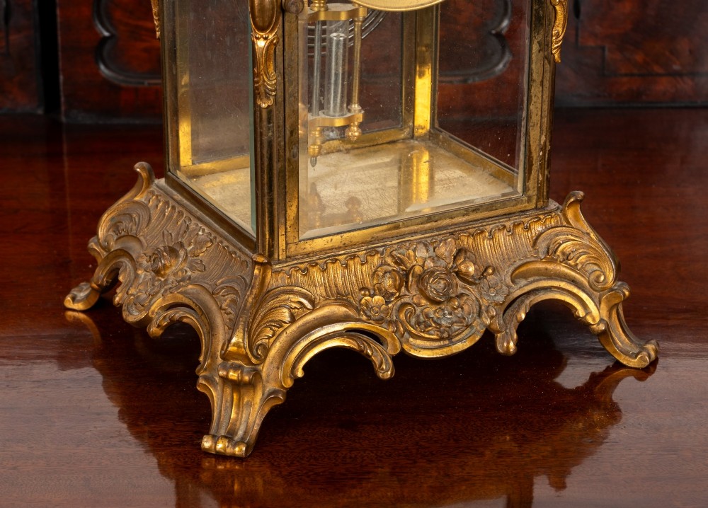 A late 19th-century Rococo Revival gilt bronze crystal regulator mantel clock featuring four bevelled glass panels, ornate scrollwork casting, an enamel dial with Roman numerals, and a visible mercury-style pendulum. View V
