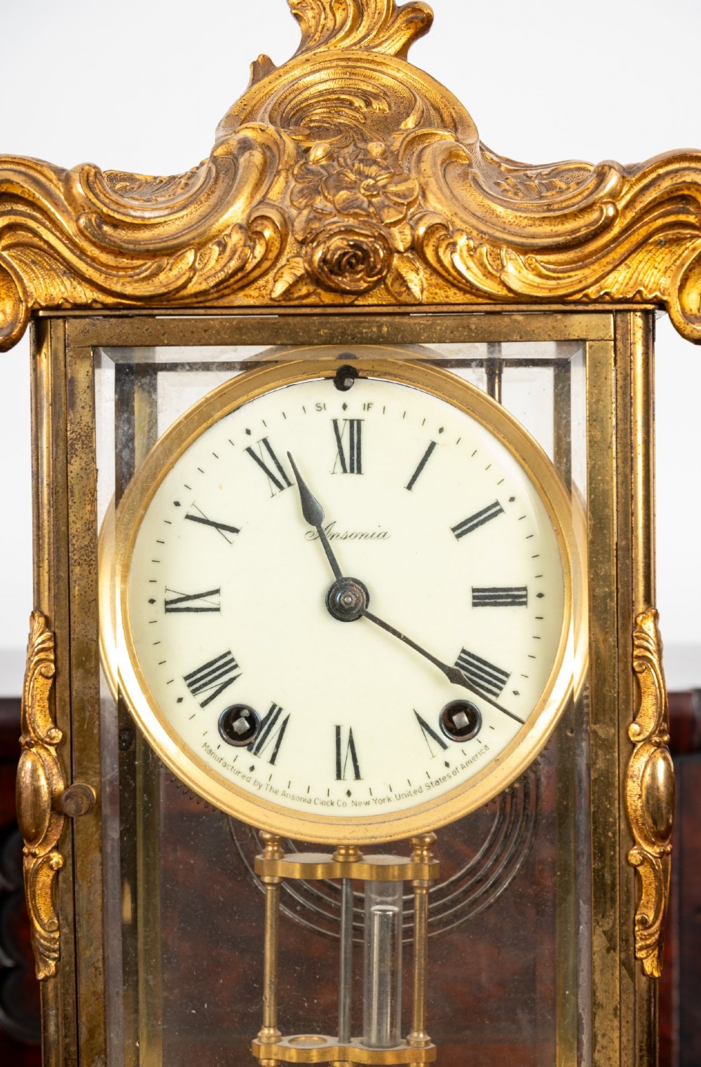 A late 19th-century Rococo Revival gilt bronze crystal regulator mantel clock featuring four bevelled glass panels, ornate scrollwork casting, an enamel dial with Roman numerals, and a visible mercury-style pendulum. View VI