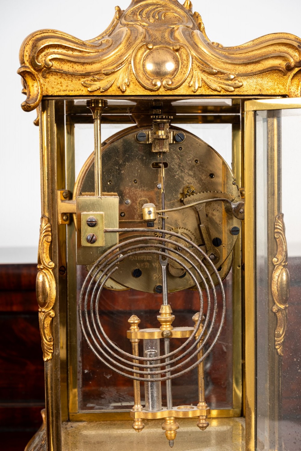 A late 19th-century Rococo Revival gilt bronze crystal regulator mantel clock featuring four bevelled glass panels, ornate scrollwork casting, an enamel dial with Roman numerals, and a visible mercury-style pendulum. View VII
