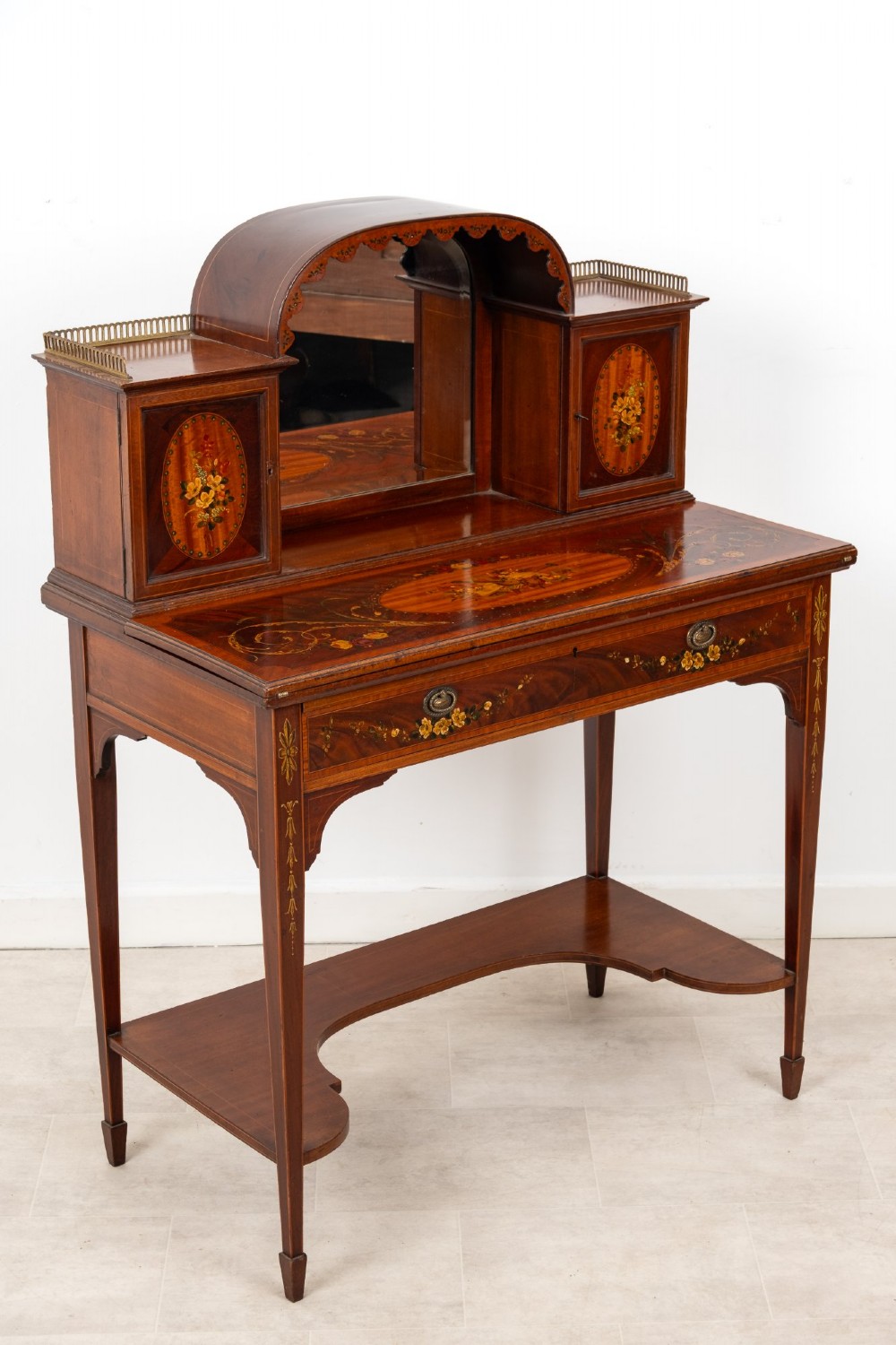 An Edwardian mahogany writing desk featuring floral hand-painted motifs, twin upper cabinets with brass galleries, an arched central mirror, and a single frieze drawer. View II