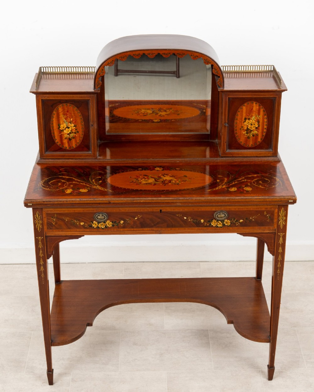 An Edwardian mahogany writing desk featuring floral hand-painted motifs, twin upper cabinets with brass galleries, an arched central mirror, and a single frieze drawer. View IV
