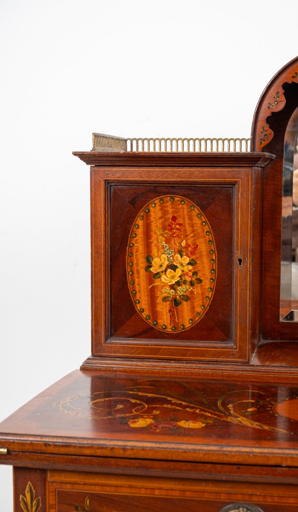 An Edwardian mahogany writing desk featuring floral hand-painted motifs, twin upper cabinets with brass galleries, an arched central mirror, and a single frieze drawer. View V