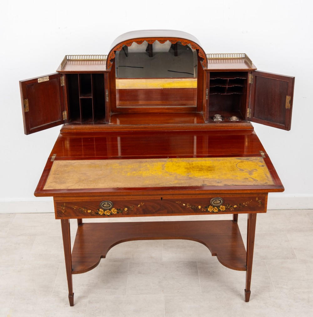 An Edwardian mahogany writing desk featuring floral hand-painted motifs, twin upper cabinets with brass galleries, an arched central mirror, and a single frieze drawer. View VIII