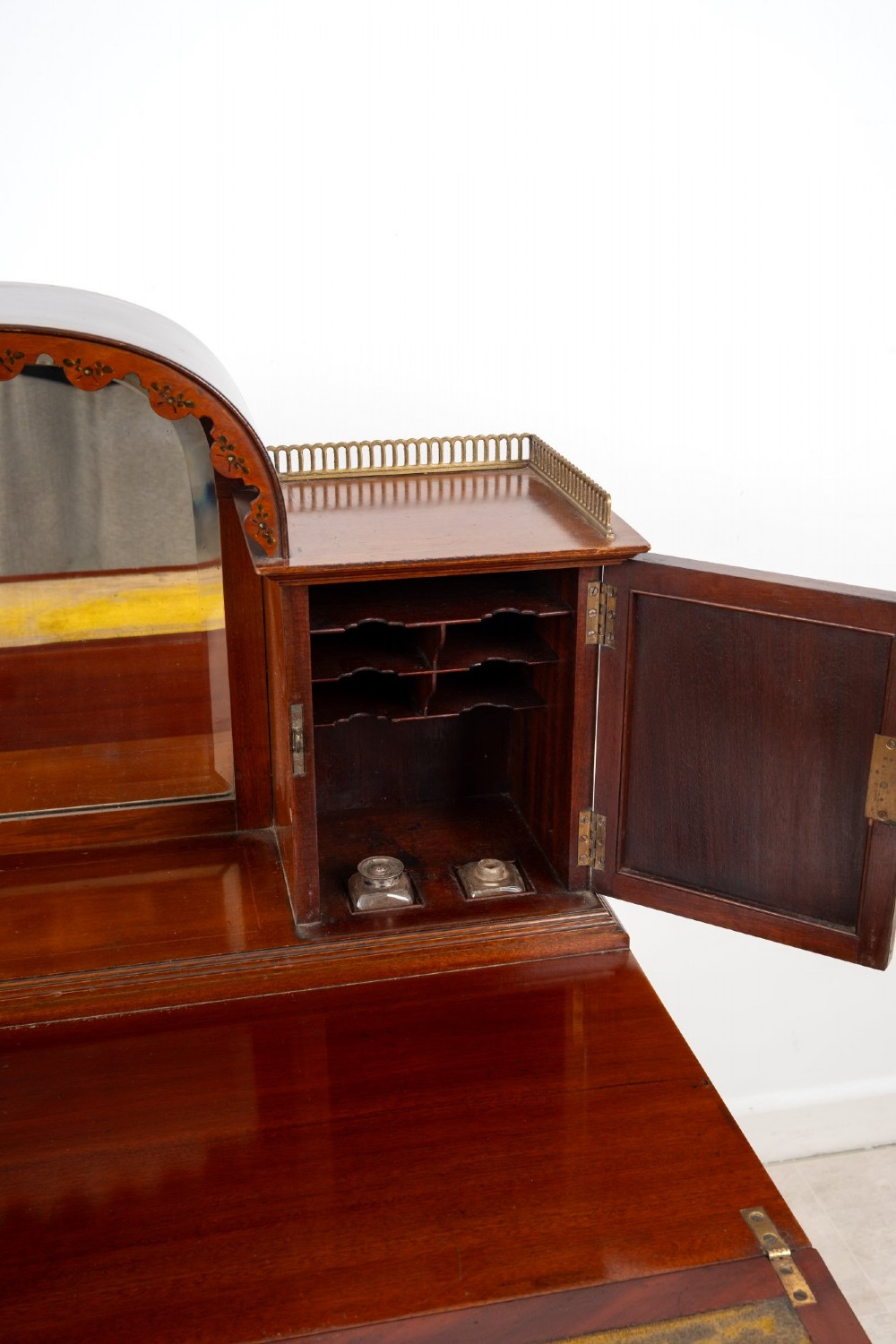 An Edwardian mahogany writing desk featuring floral hand-painted motifs, twin upper cabinets with brass galleries, an arched central mirror, and a single frieze drawer. View X