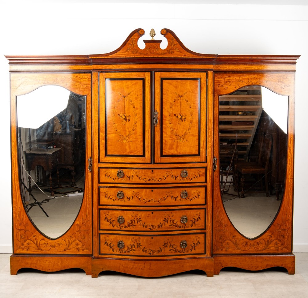 An Edwardian satinwood compactum wardrobe featuring twin arched mirror doors flanking a central cupboard and bank of four drawers, topped with a scroll pediment. View II