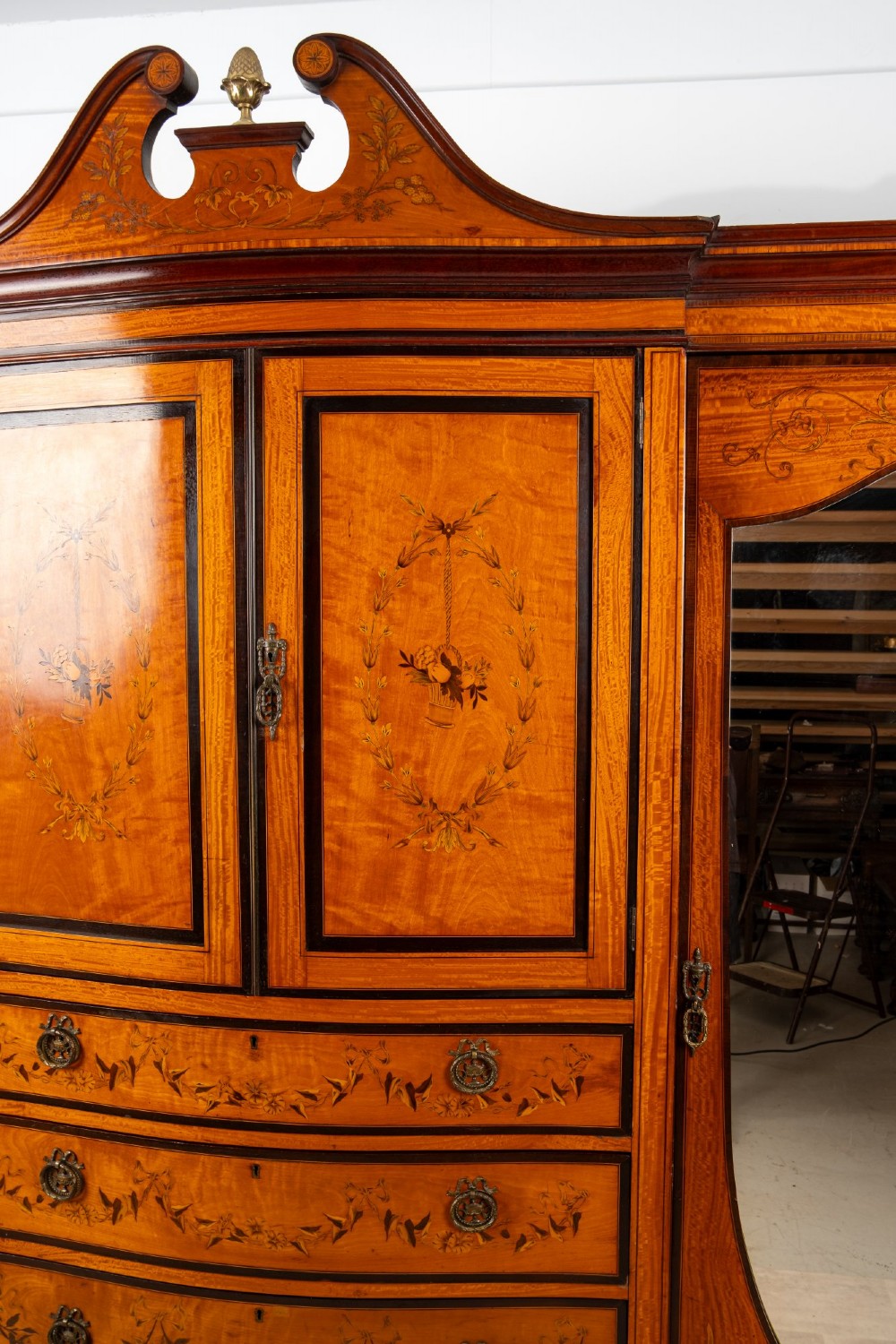 An Edwardian satinwood compactum wardrobe featuring twin arched mirror doors flanking a central cupboard and bank of four drawers, topped with a scroll pediment. View III