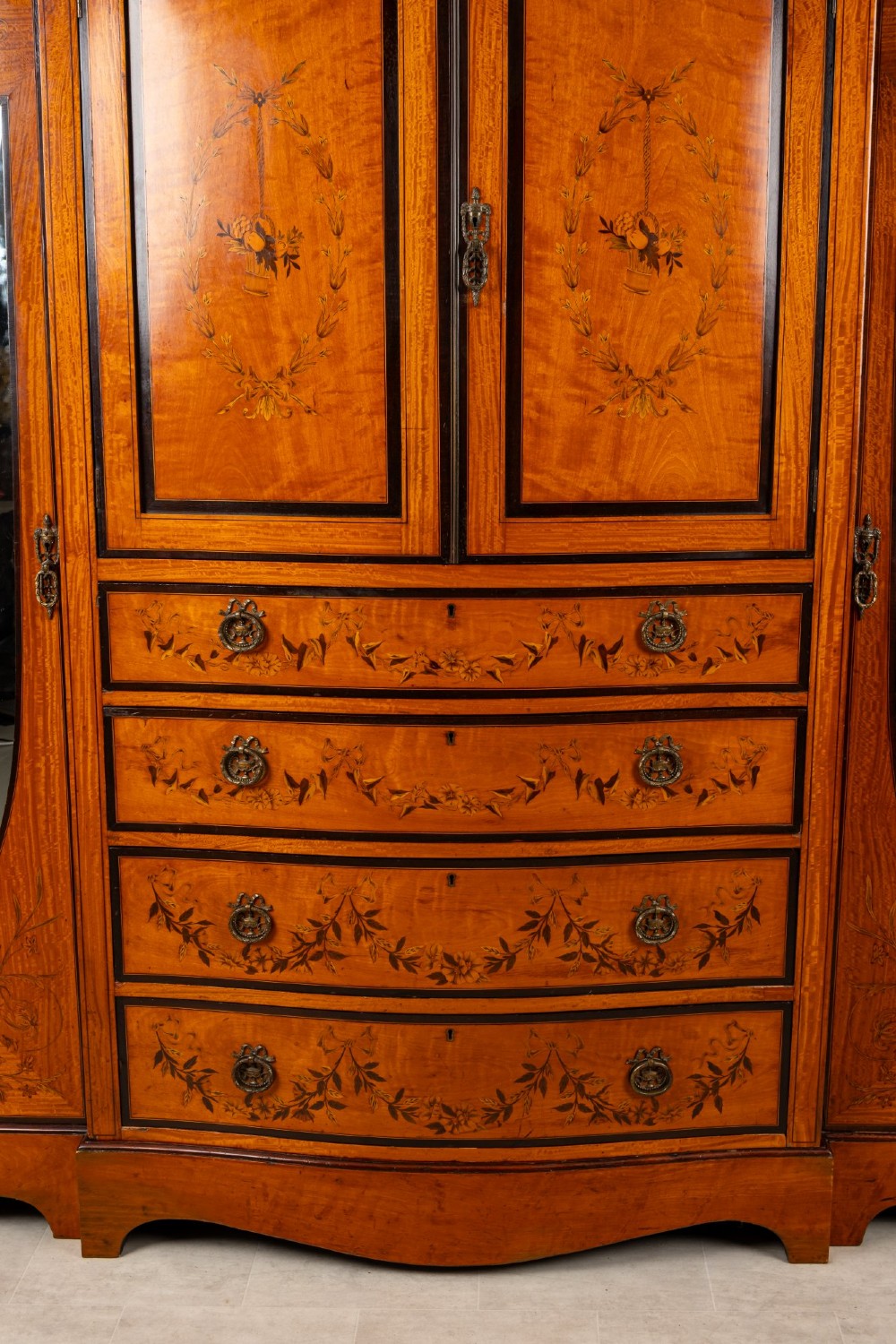 An Edwardian satinwood compactum wardrobe featuring twin arched mirror doors flanking a central cupboard and bank of four drawers, topped with a scroll pediment. View IV