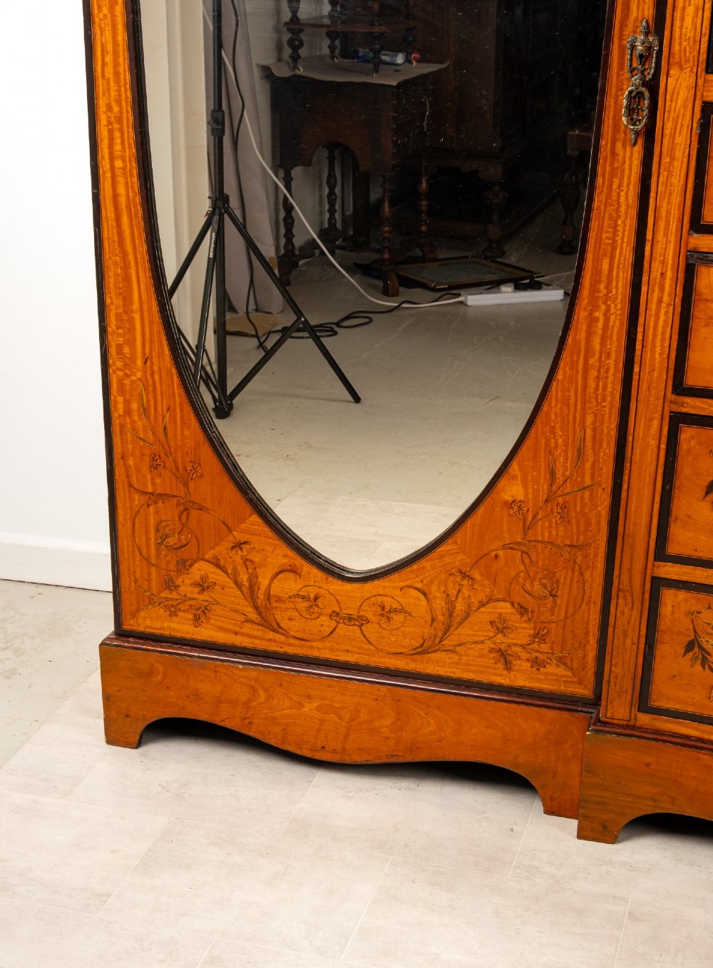 An Edwardian satinwood compactum wardrobe featuring twin arched mirror doors flanking a central cupboard and bank of four drawers, topped with a scroll pediment. View V