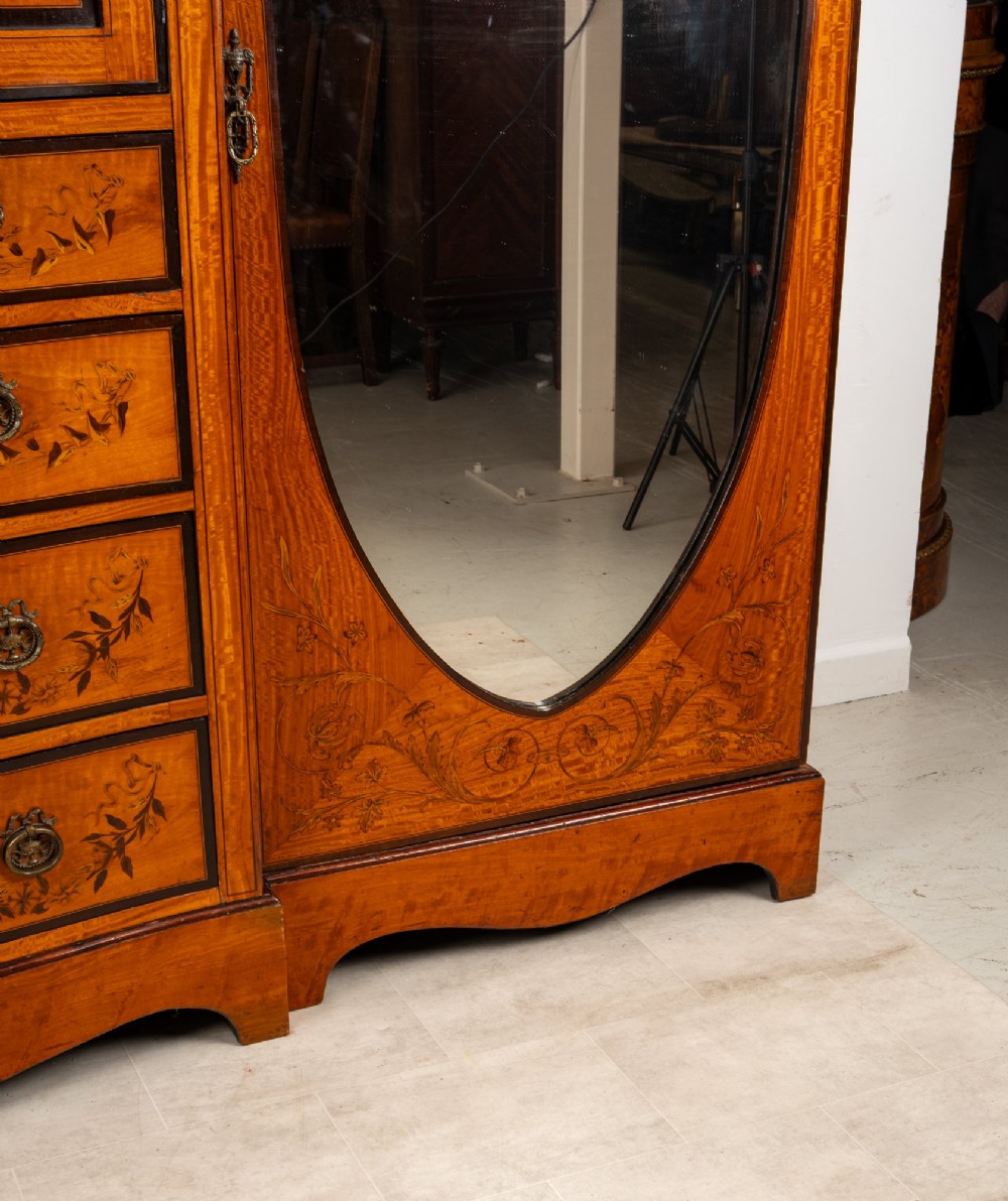 An Edwardian satinwood compactum wardrobe featuring twin arched mirror doors flanking a central cupboard and bank of four drawers, topped with a scroll pediment. View VI