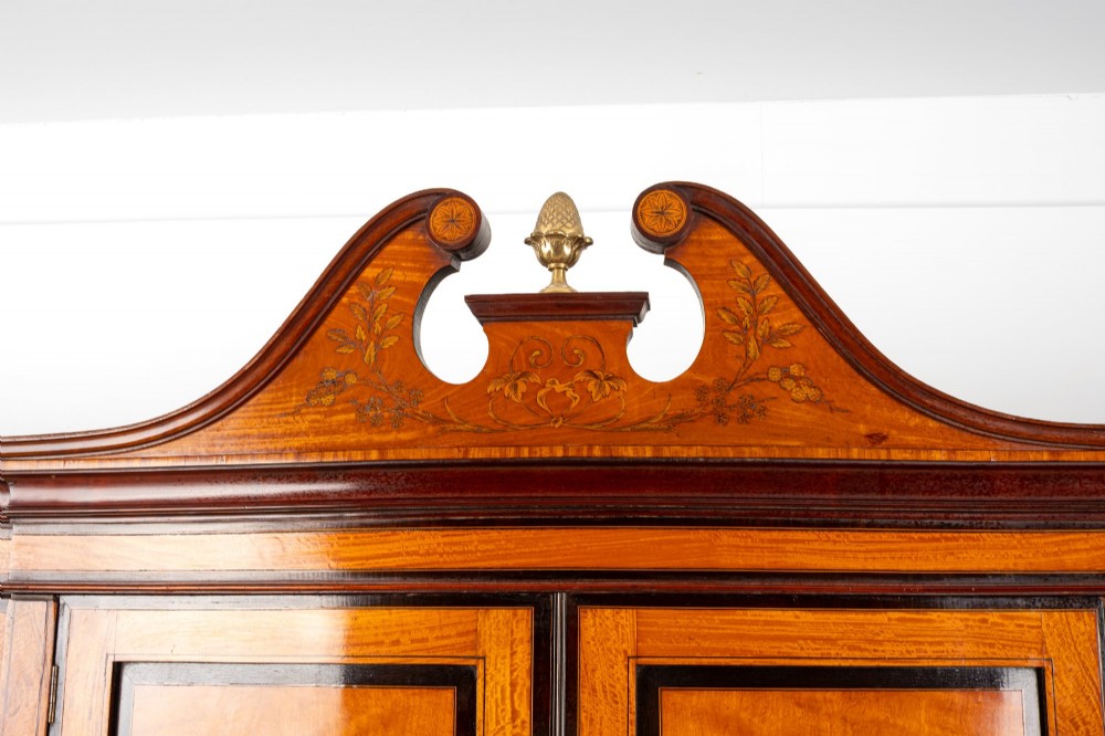 An Edwardian satinwood compactum wardrobe featuring twin arched mirror doors flanking a central cupboard and bank of four drawers, topped with a scroll pediment. View VII