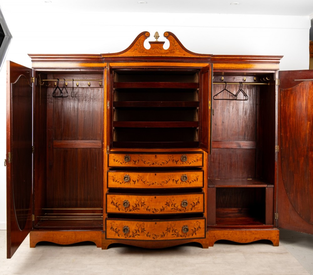 An Edwardian satinwood compactum wardrobe featuring twin arched mirror doors flanking a central cupboard and bank of four drawers, topped with a scroll pediment. View VIII