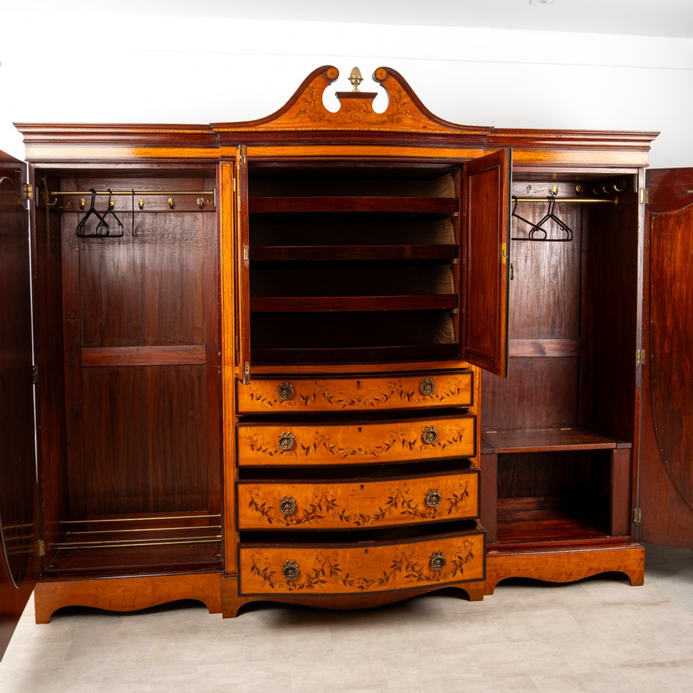 An Edwardian satinwood compactum wardrobe featuring twin arched mirror doors flanking a central cupboard and bank of four drawers, topped with a scroll pediment. View IX