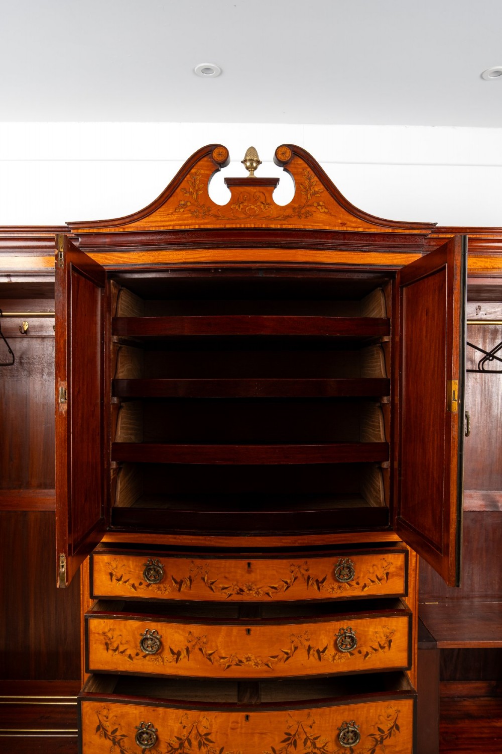 An Edwardian satinwood compactum wardrobe featuring twin arched mirror doors flanking a central cupboard and bank of four drawers, topped with a scroll pediment. View X
