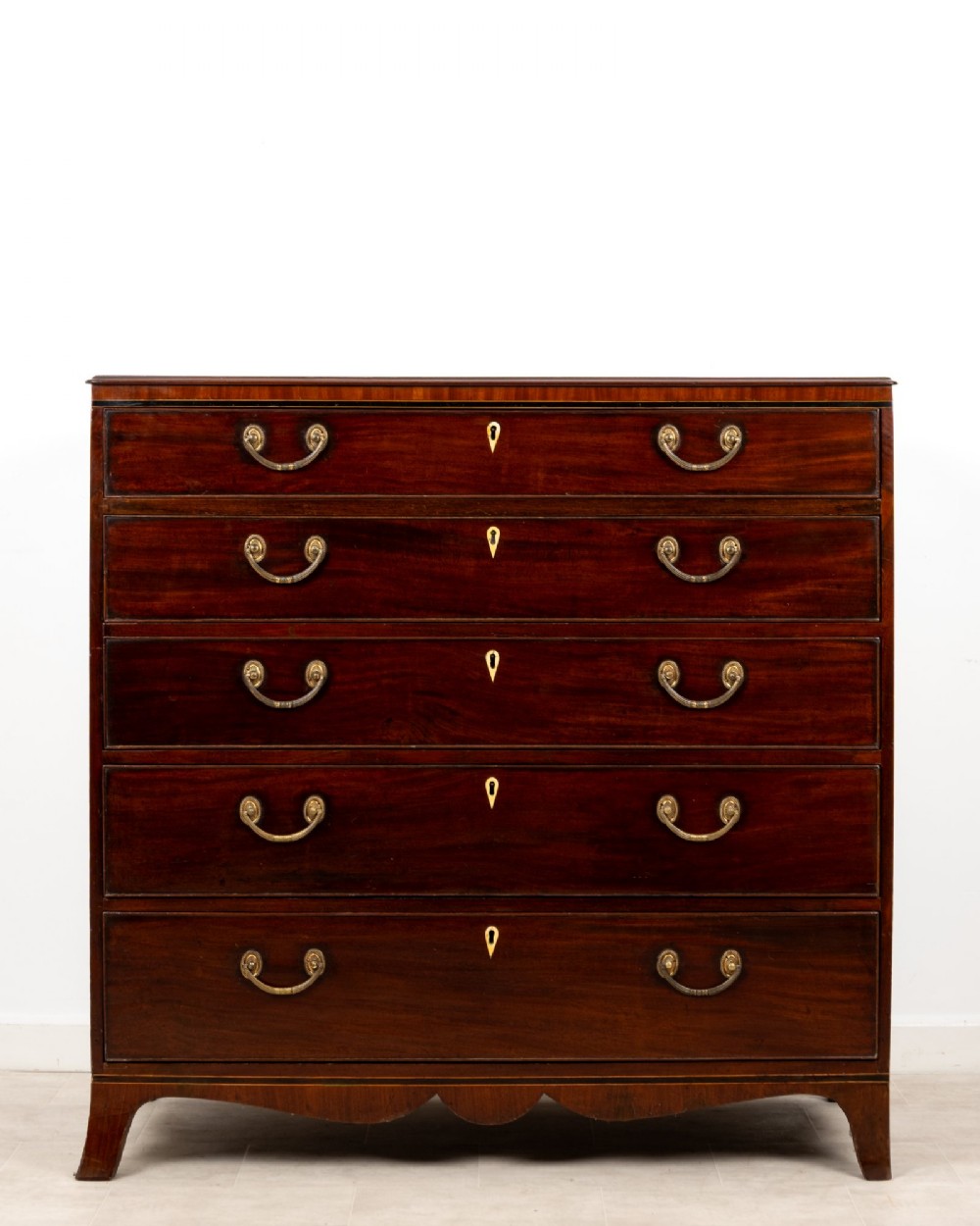 A nineteenth-century mahogany chest of five drawers featuring brass drop handles, keyhole escutcheons, and a shaped lower apron.