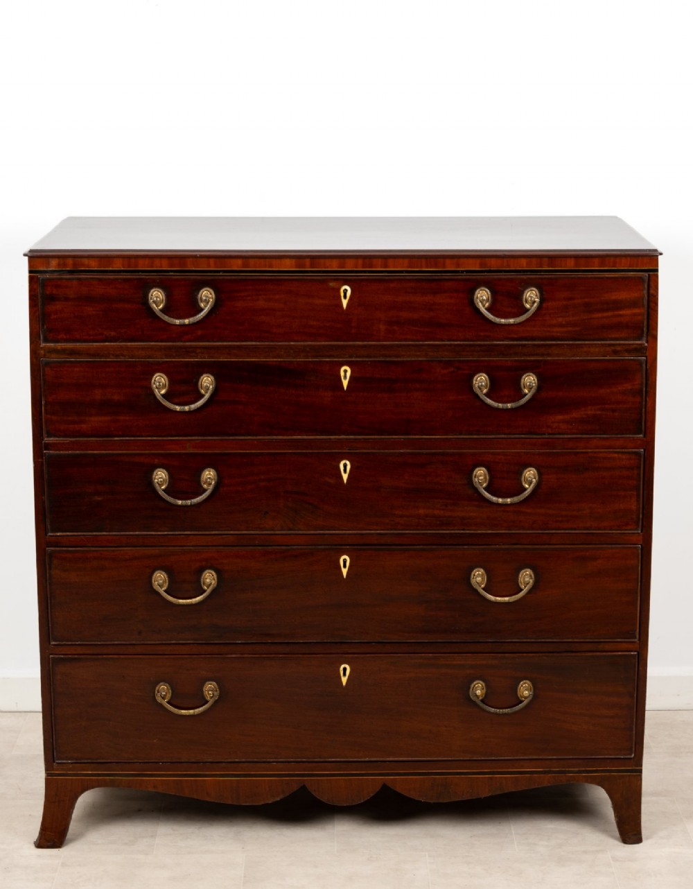 A nineteenth-century mahogany chest of five drawers featuring brass drop handles, keyhole escutcheons, and a shaped lower apron. View II