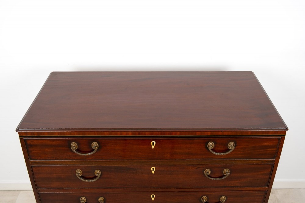 A nineteenth-century mahogany chest of five drawers featuring brass drop handles, keyhole escutcheons, and a shaped lower apron. View V
