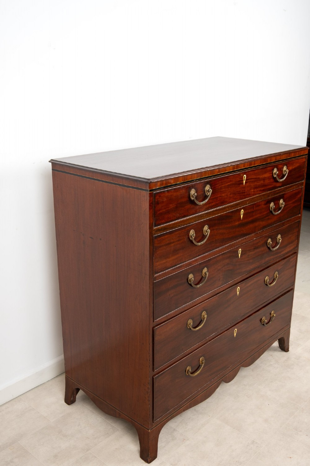 A nineteenth-century mahogany chest of five drawers featuring brass drop handles, keyhole escutcheons, and a shaped lower apron. View VII