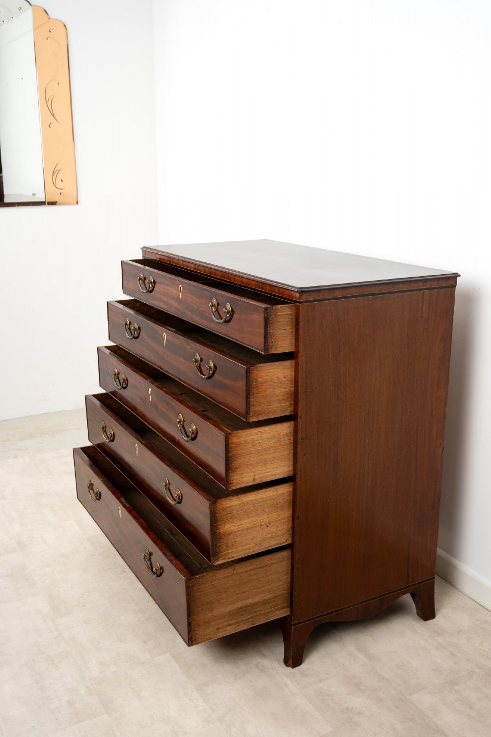 A nineteenth-century mahogany chest of five drawers featuring brass drop handles, keyhole escutcheons, and a shaped lower apron. View VIII