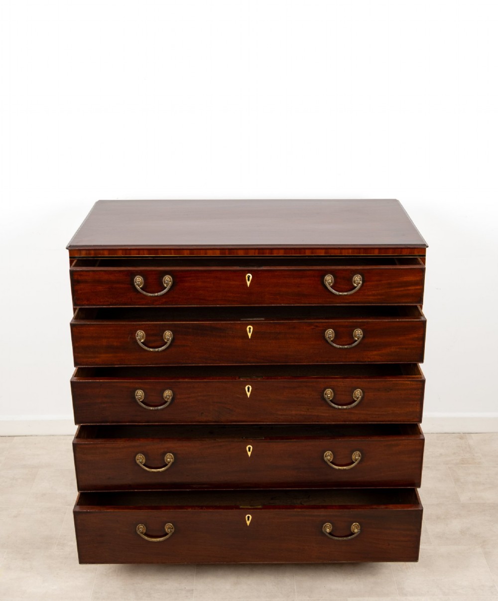 A nineteenth-century mahogany chest of five drawers featuring brass drop handles, keyhole escutcheons, and a shaped lower apron. View IX