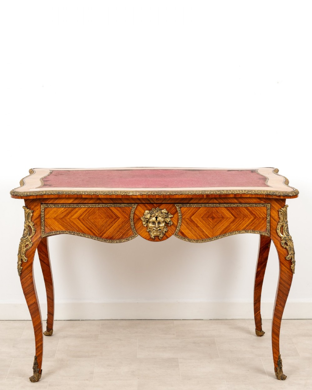 A late 19th-century French kingwood bureau plat featuring a red leather inset top, geometric parquetry veneer, ormolu mounts, and cabriole legs.