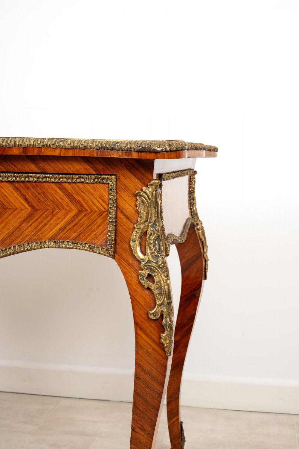 A late 19th-century French kingwood bureau plat featuring a red leather inset top, geometric parquetry veneer, ormolu mounts, and cabriole legs. View VI