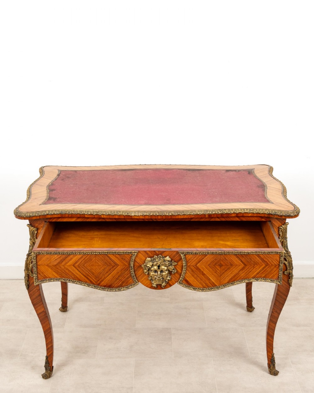 A late 19th-century French kingwood bureau plat featuring a red leather inset top, geometric parquetry veneer, ormolu mounts, and cabriole legs. View VII