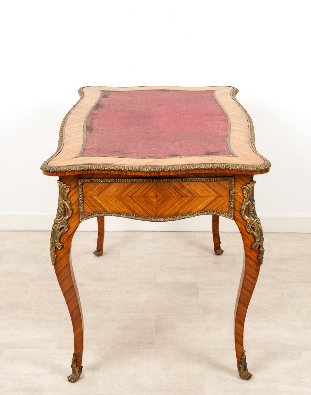 A late 19th-century French kingwood bureau plat featuring a red leather inset top, geometric parquetry veneer, ormolu mounts, and cabriole legs. View IX