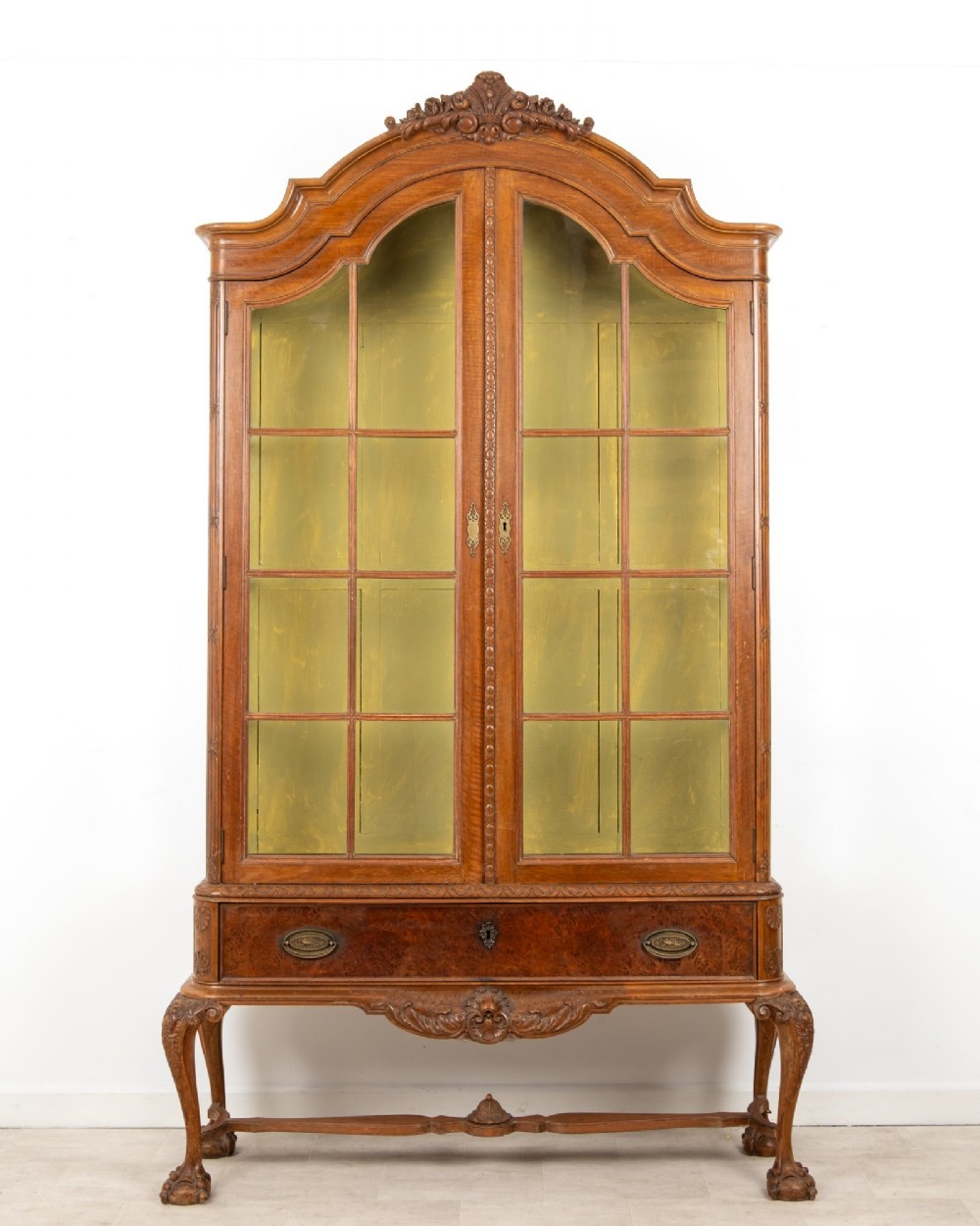 A Queen Anne Revival walnut display cabinet featuring a shaped pediment, double glazed doors, a single lower drawer, and carved cabriole legs.