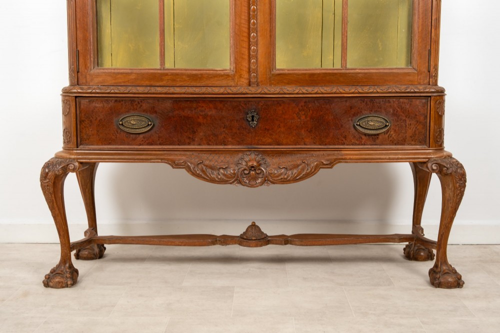 A Queen Anne Revival walnut display cabinet featuring a shaped pediment, double glazed doors, a single lower drawer, and carved cabriole legs. View IV
