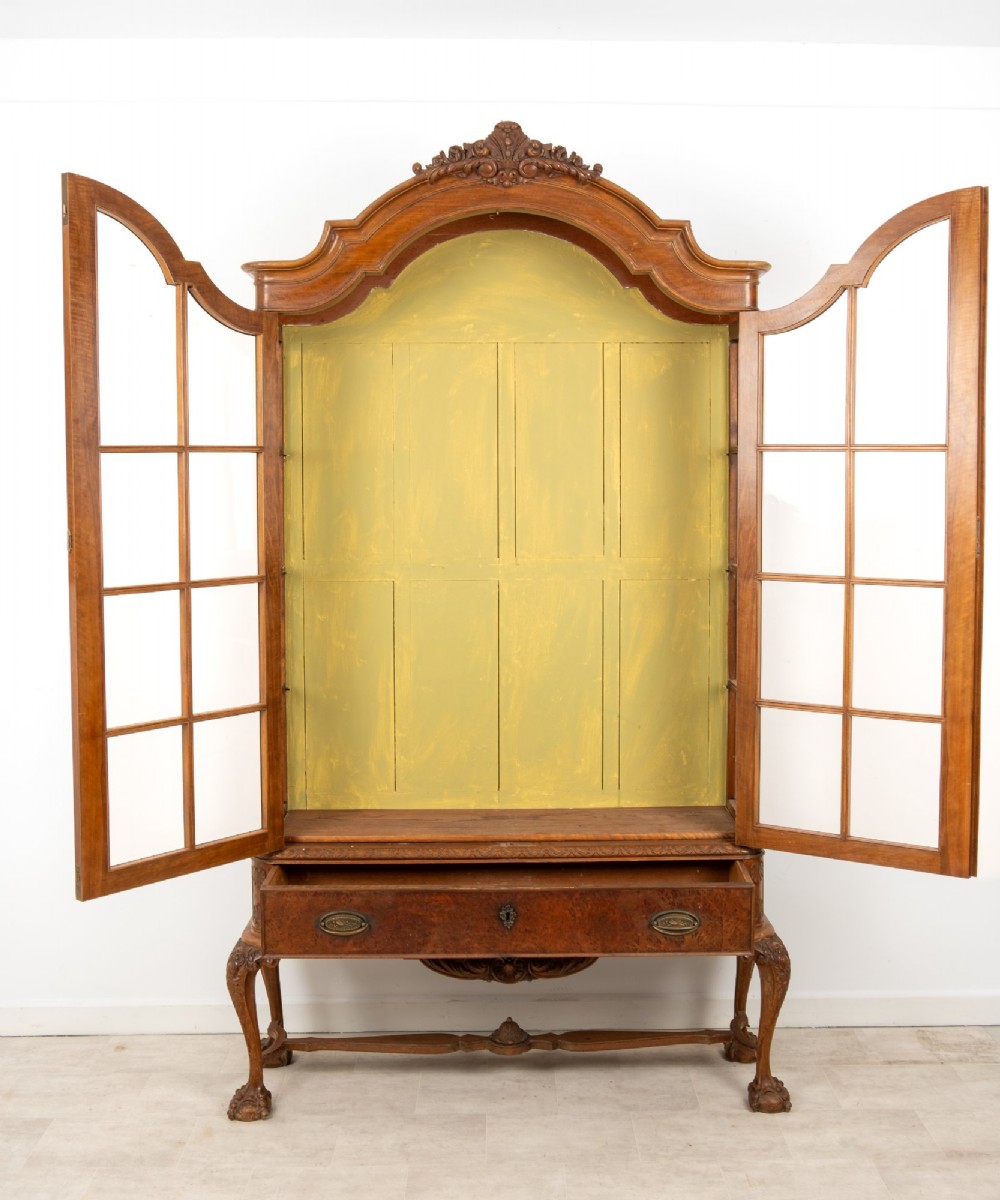 A Queen Anne Revival walnut display cabinet featuring a shaped pediment, double glazed doors, a single lower drawer, and carved cabriole legs. View VIII