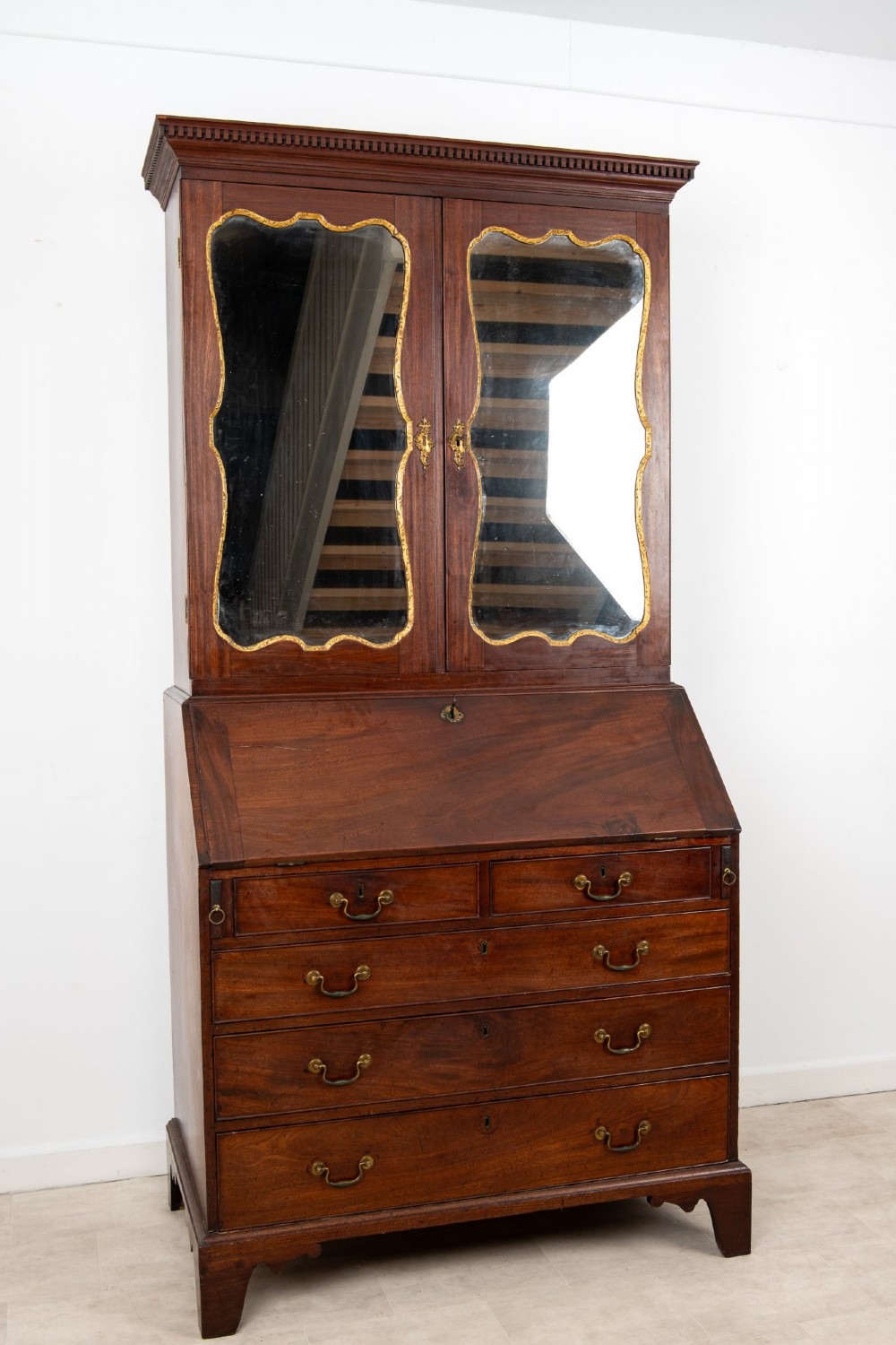 An eighteenth-century mahogany bureau bookcase featuring shaped mirrored double doors on the upper cabinet, a slant-front desk midsection, and four graduated drawers below with brass drop handles. View IV